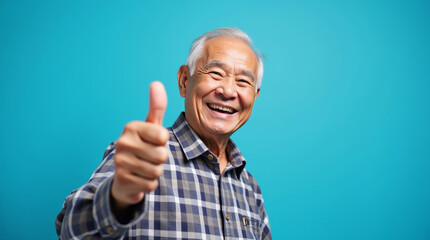 Happy senior man in plaid shirt showing thumbs up on blue background, positive expression and approval gesture
