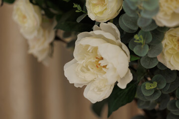 Elegant white flowers with green eucalyptus in a white vase, set against beige patterned curtains. Neutral tones. Suitable for wedding, celebration, luxury decor, floral arrangement concepts.