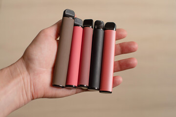Various disposable electronic cigarettes in a female hand on a light background