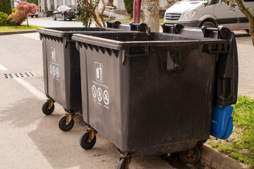 Large black garbage containers line the road on a city street in Georgia