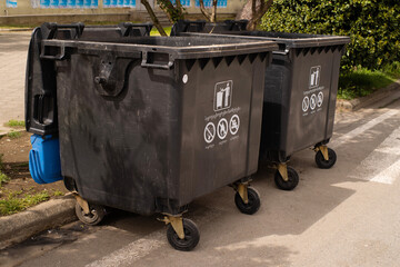 Large black garbage containers line the road on a city street in Georgia