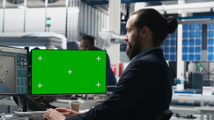 Young business specialist uses computer with green screen and production metrics, overseeing the industrial operations and high tech equipment. Master engineer works on sustainability. Camera B.