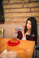 A beautiful girl in a wine-colored dress is sending photos from her phone while smiling at her...