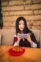 A beautiful girl in a wine-colored dress is sending photos from her phone while smiling at her...