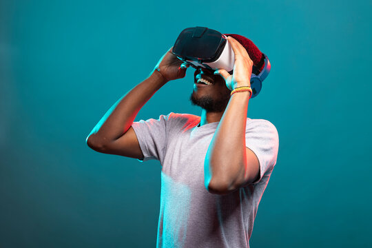 Black male model playing an interactive VR game, engaged in a futuristic 3D simulation, adjusting his headset. African american man looking upward and exploring a virtual reality world. - Powered by Adobe
