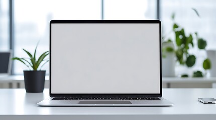 A silver laptop with a blank white screen placed on a clean white desk in a minimalist office setup. Background includes a potted plant and a blurred window view.