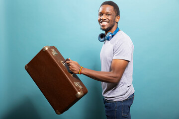 Cheerful male traveler swinging his suitcase, filled with excitement and ready for vacation. Black...