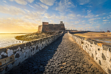Sunset view of the Castillo de San Gabriel or Castle of San Gabriel, a 16th century fortress extending into the bay of Arrecife, in Arrecife Spain on the Canary island of Lanzarote.	