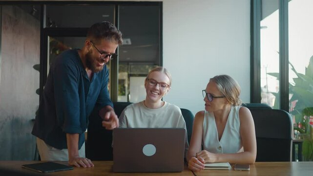 Three happy colleagues are giving high five to each other in office, celebrating their success after completing project using laptop. Concept Successful completion of transaction by sales team