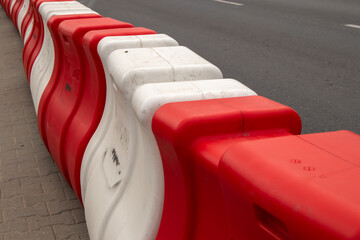 Red and white plastic road barriers used for traffic control and construction site safety. Urban street infrastructure element close-up
