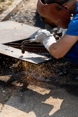 Skilled welder performs metal cutting in workshop during bright daylight with sparks flying