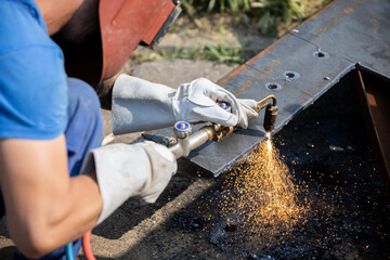 Man performs welding on metal surface outdoors during daylight using equipment to create sparks