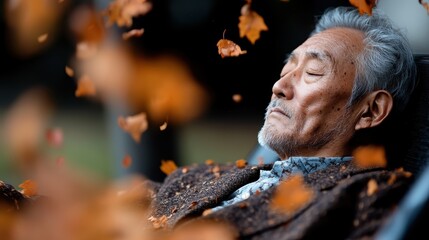 An elderly man enjoys a moment of tranquility while resting with eyes closed as vibrant autumn leaves fall around him, symbolizing peace and reflection.