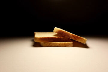 Three slices of white sandwich bread stacked on a white surface with dramatic lighting and dark background, minimalistic food concept