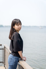 A young teenager girl stands comfortably on a sunlit wooden bridge, casually dressed in a black top, jeans, and black boots.