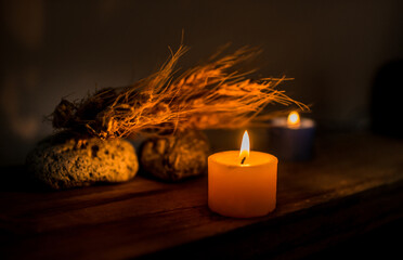 Velas encendidas junto a espigas de trigo y piedras sobre mesa de madera en ambiente cálido y...