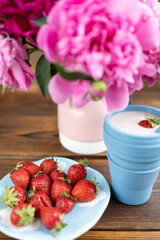A glass of strawberry milkshake. Pink peonies and red strawberries
