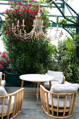 A cozy outdoor seating area with four rattan chairs and a round table surrounded by lush green plants and vibrant flowers