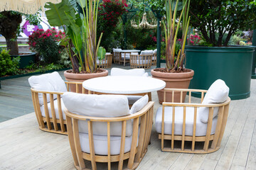 A cozy outdoor seating area with four rattan chairs and a round table surrounded by lush green plants and vibrant flowers