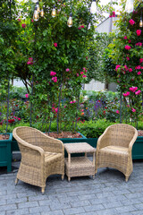 A cozy outdoor seating area with four rattan chairs and a round table surrounded by lush green plants and vibrant flowers