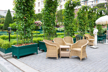 A cozy outdoor seating area with four rattan chairs and a round table surrounded by lush green plants and vibrant flowers