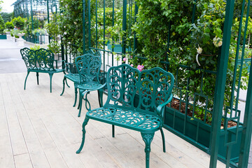 A modern outdoor seating area with green metal chairs and tables. lush greenery, recreation area.