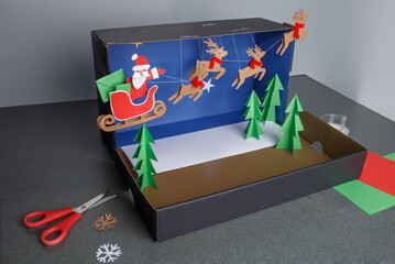 a step-by-step visual guide for making a Christmas-themed diorama using paper crafts. shoebox as the base and decorating it with colored paper, A fun, creative, and simple DIY holiday project