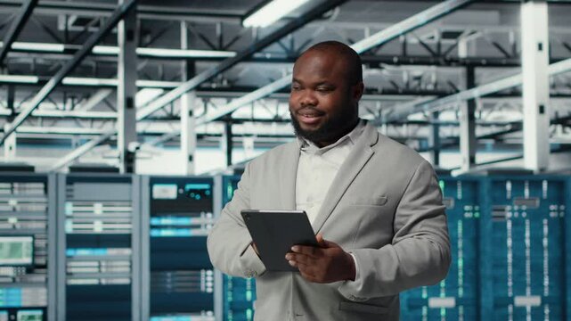 Cheerful data center programmer looking at code debugging tools running on tablet. Server farm IT professional typing on device touchscreen, writing script automating tasks, camera B
