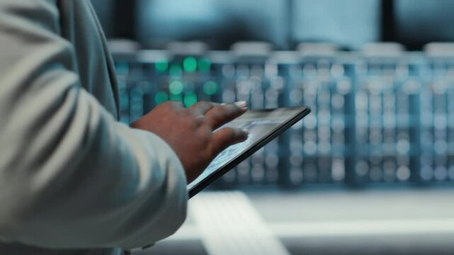 Manager walking in server hub using tablet to find firewall misconfigurations affecting rackmounts performance. Admin checking systems bottlenecks leading to sluggish data transfer rates, camera B