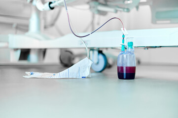 Tube connected to a gravity drainage device on a hospital room floor containing serum and blood from a patient after surgery. Essential medical equipment for monitoring postoperative fluid output.