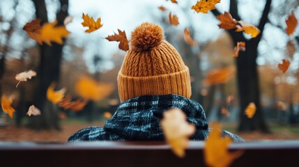 A serene autumn scene captures a person in a yellow beanie, sitting on a bench as leaves gracefully fall around them, evoking feelings of tranquility and nostalgia.