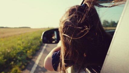 little girl dreams car window, following the road into the sunset. wind plays with hair,...