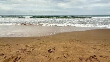A tranquil and serene beach landscape featuring soft, golden sand, gentle waves, and overcast grey skies