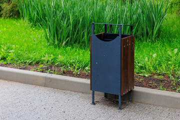 Urban outdoor trash bin by lush greenery on a paved street