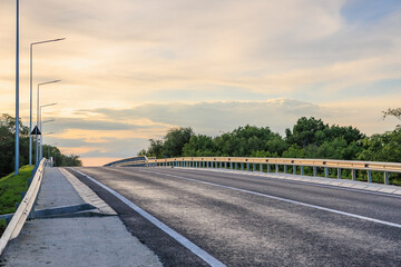 Scenic empty highway with lush greenery and dramatic sky at sunset