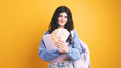 University student holding euro banknotes and school books on yellow background
