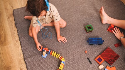Obraz premium Child playing with colorful toys and listening music with headphones on a carpet
