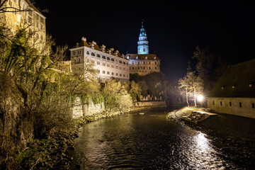 Fototapeta premium Nighttime view of historic Cesky Krumlov castle alongside illuminated riverbank