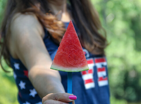 Latino woman wearing USA patriotic colors holding a watermelon piece during a July 4th outdoor party celebrating freedom. 