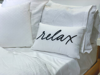 White of bed with white sheets and a pillow with the word relax written on it, suitable for...
