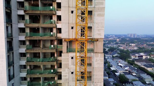 Aerial footage captures a building under construction with a yellow crane. The camera pans up to reveal the city skyline and nearby residential area at sunrise.
