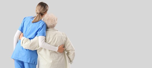 Senior woman with nurse hugging on light background with space for text, back view