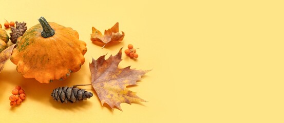 Pumpkin, cone, berries and autumn leaves on yellow background with space for text