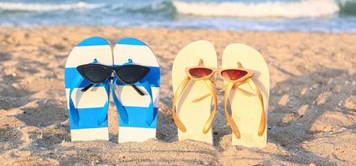 Stylish sunglasses with colorful pairs of flip-flops on sand