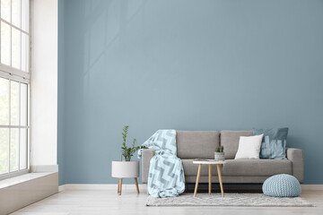 Interior of light living room with grey sofa, table and pouf