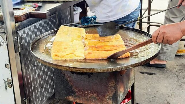 A seller's hand is frying egg martabak in a special frying pan. Egg martabak is one of Indonesia's typical foods.