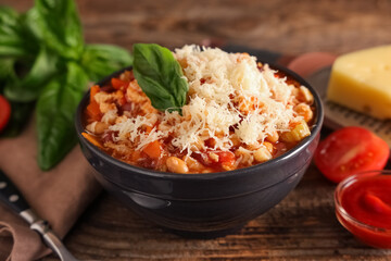 Bowl of pasta fagioli with cheese and basil on wooden background