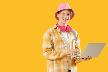Male student using laptop on yellow background
