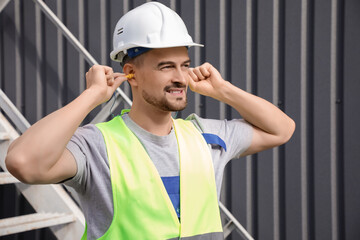Male builder putting in earplugs outdoors