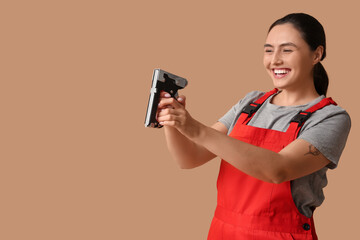 Young female construction worker with industrial stapler on beige background. Woman in male...